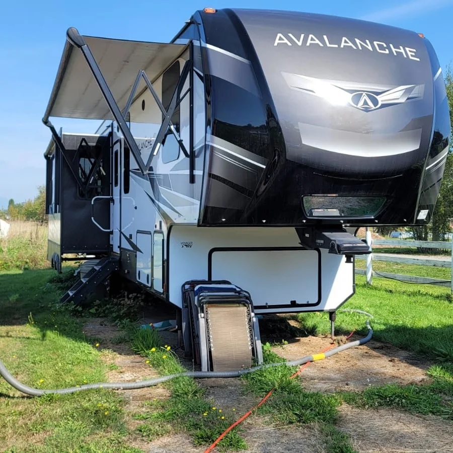 Large fifth-wheel RV parked on grass with tank-service hose set up at the site.